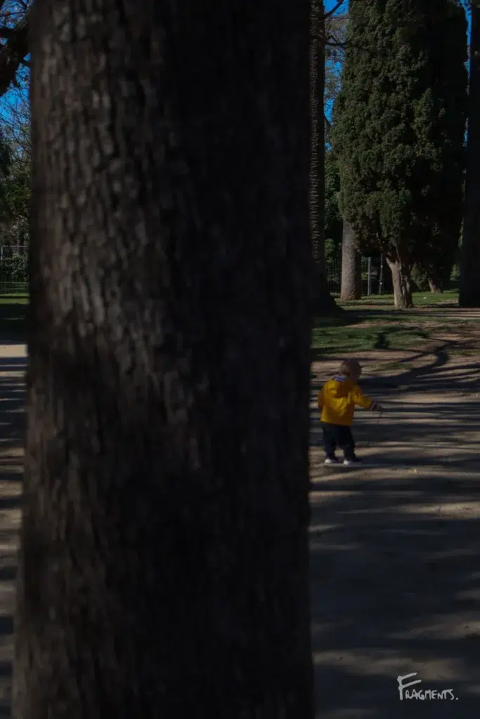 Voyage poétique et photographique à travers Barcelone : Enfant au manteau jaune tenant un bâton à la main dans un parc