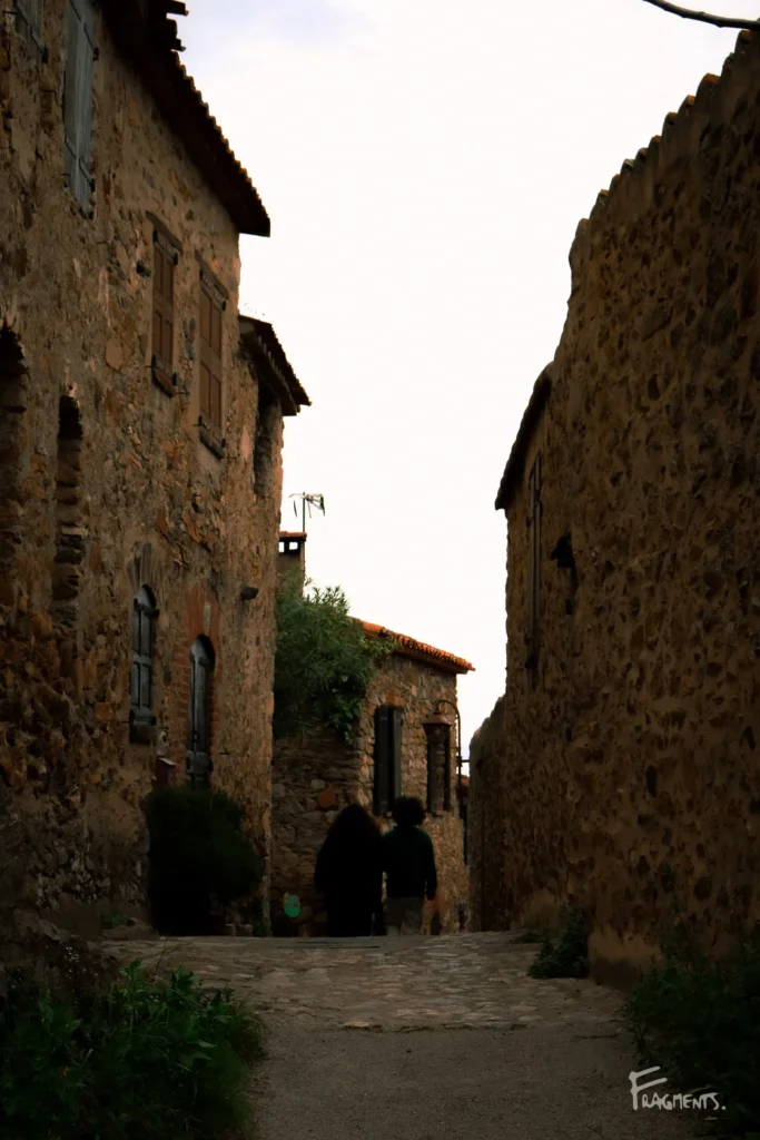 Voyage poétique et photographique à travers Castelnou : Couple marchant de dos dans une ruelle du village en pierres dans les Pyrénées-Orientales