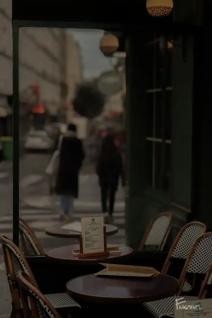 Voyage poétique et photographique à travers Paris : Terrasse de café vide avec à travers la vitre, un couple marchant