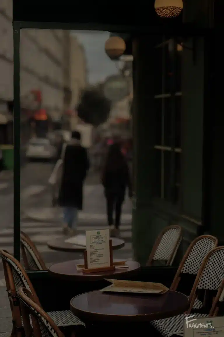 Voyage poétique et photographique à travers Paris : Terrasse de café vide avec à travers la vitre, un couple marchant